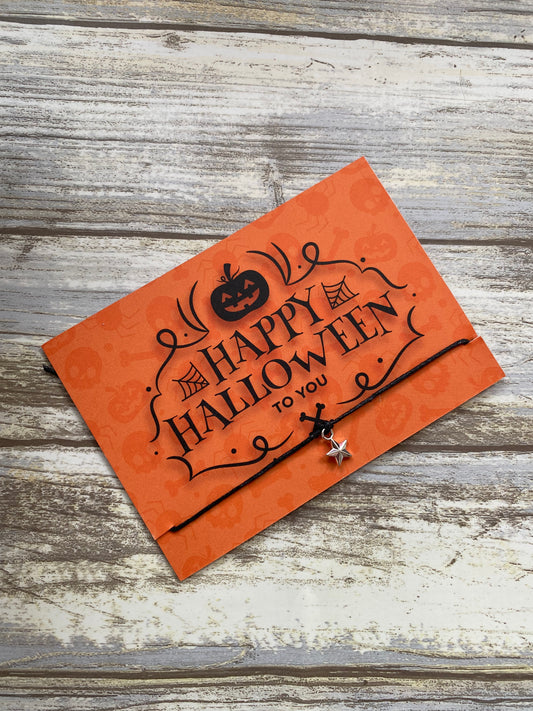 An orange wish bracelet with 'Happy Halloween' and 'To You' text, featuring a pumpkin design, presented on a wooden background.