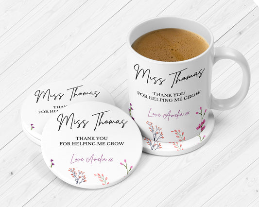 White ceramic mug and coasters set with the name “Miss Thomas” and the message “Thank you for helping me grow. Love Amelia xx.” Decorated with delicate floral illustrations in pink, purple, and coral tones. Displayed on a white wooden surface.