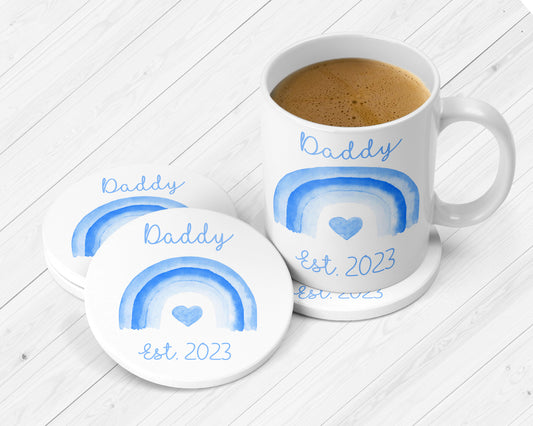 A set of personalised tableware with a mug and a white ceramic coaster, both featuring a blue 'Daddy' text and a heart symbol graphic.