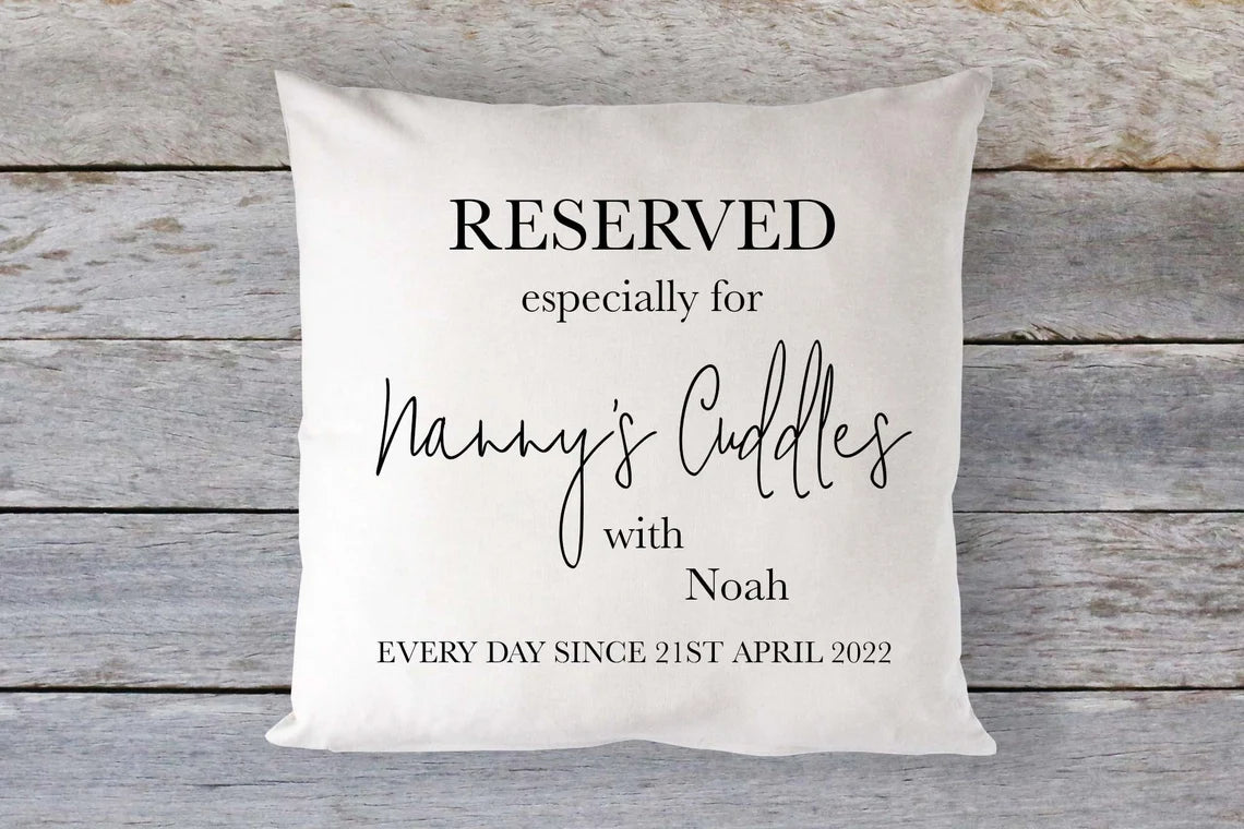 A square-shaped cushion with a linen cover, featuring personalised text that reserves it 'especially for Nanny's Cuddles' with a name and date.