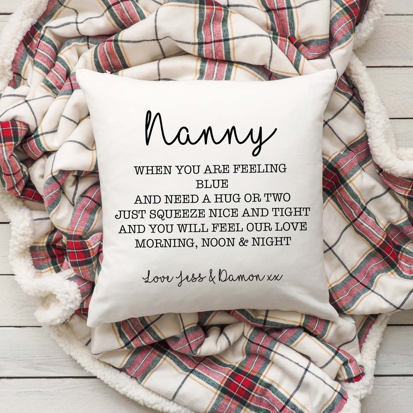 A linen cushion with the word 'Nanny' printed on it, placed on a checkered blanket with a personalised message.