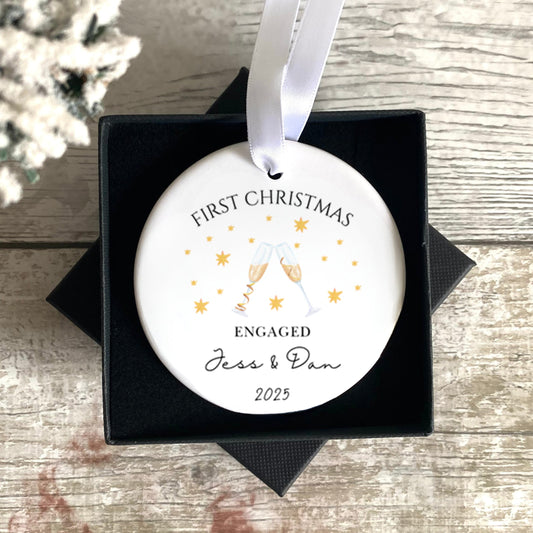 Personalised First Christmas Engaged ornament in a black box on a wooden surface with a snowy background.