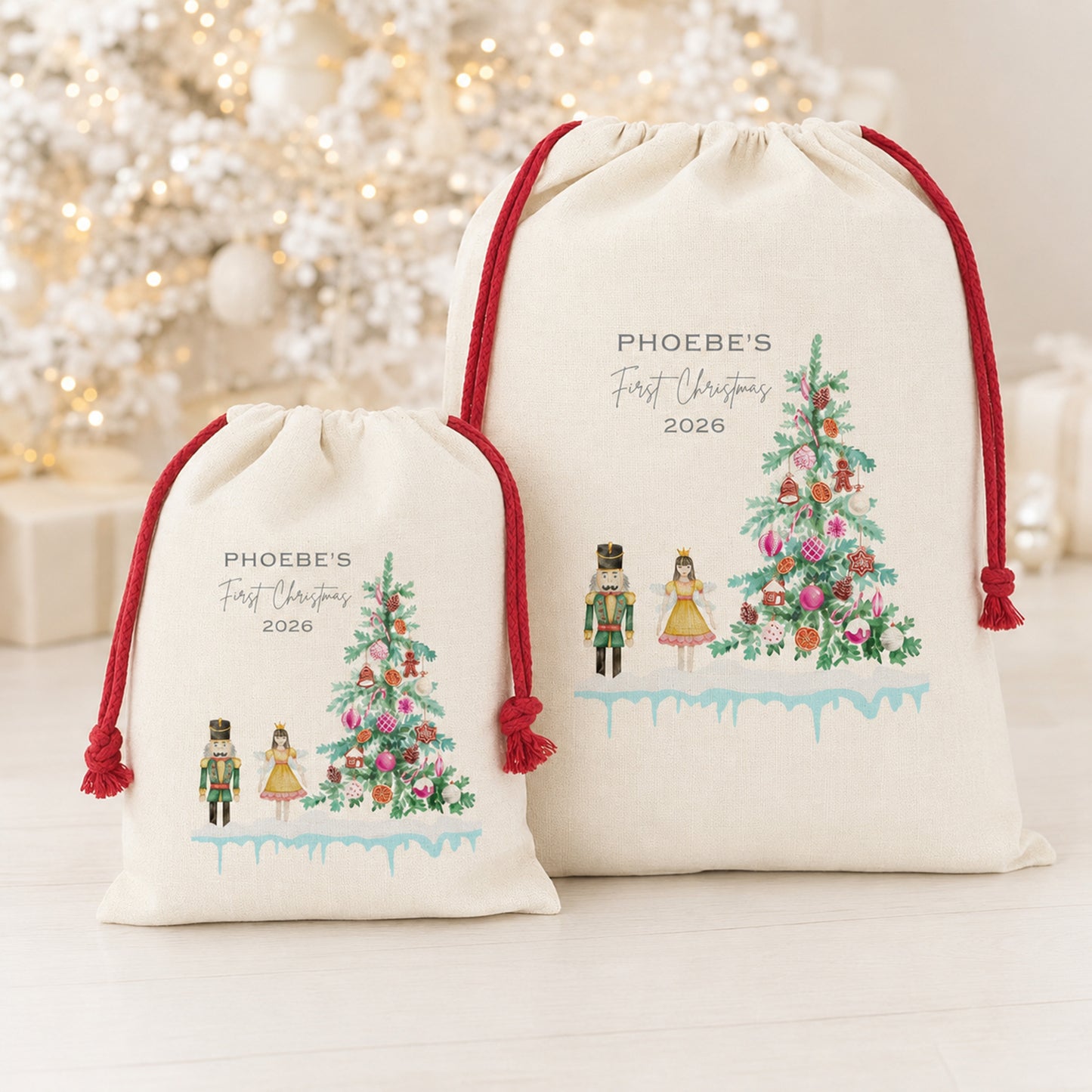 Two personalized cream-colored drawstring gift bags with red cords, featuring a watercolor Christmas tree and nutcracker design, displayed in front of a blurred festive background.