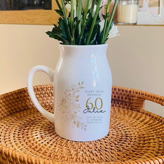 White 60th birthday vase pitcher with floral arrangement on a woven tray in a home setting