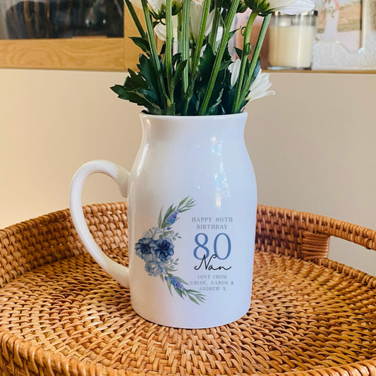 White 80th birthday vase pitcher with floral design on a woven tray with flowers