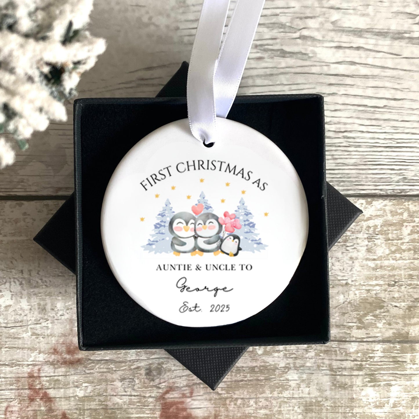 Personalised Christmas ornament in a black box on a wooden surface with a snowy background.