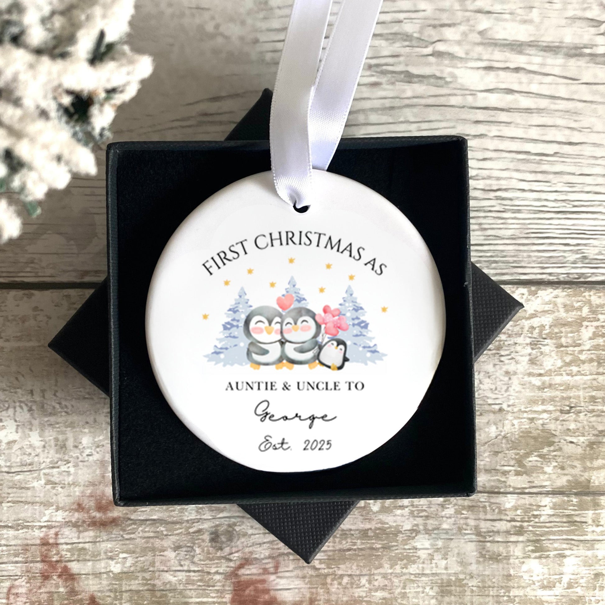 Personalised Christmas ornament in a black box on a wooden surface with a snowy background.