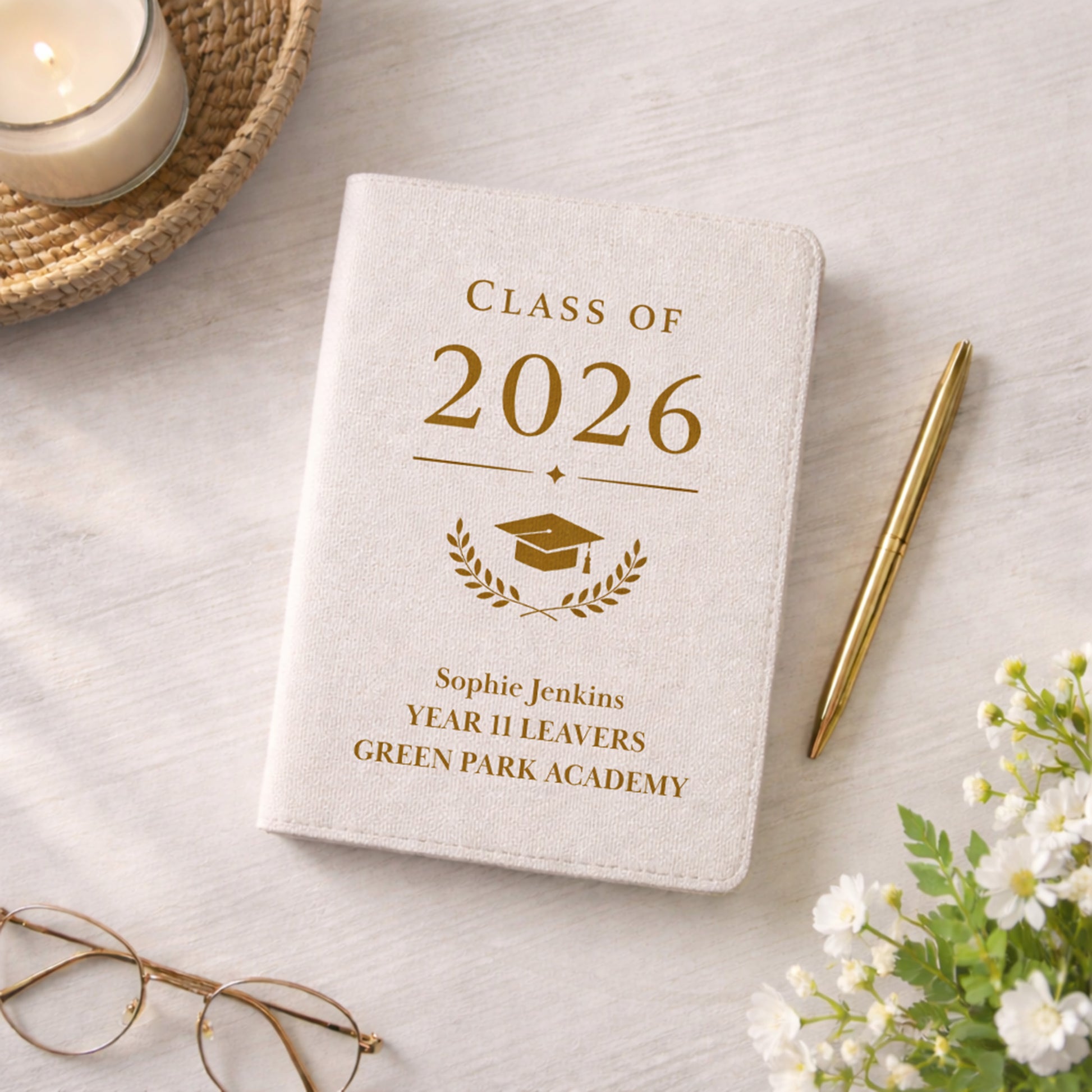 Notebook with 'Class of 2026' design on a light surface with a candle, pen, and flowers.
