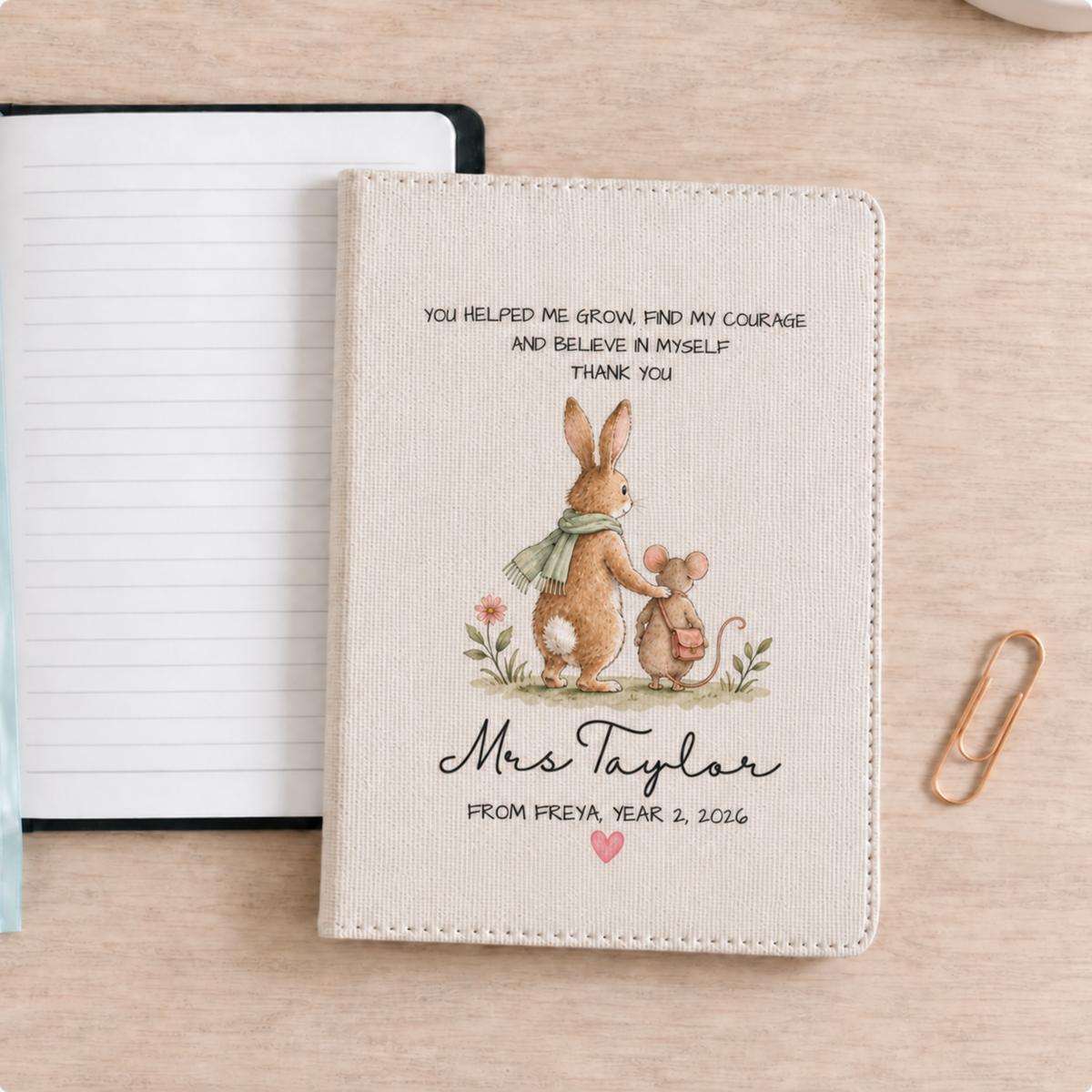 A personalized faux linen notebook cover featuring a watercolor illustration of a rabbit and a mouse with a thank you message, displayed on a light wood desk next to a lined notebook and a gold paperclip.