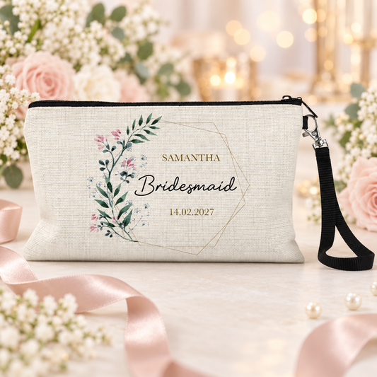 A personalised wedding day cream-colored linen wristlet clutch with a black wrist strap, featuring a floral wreath design and the text 'Samantha Bridesmaid 14.02.27