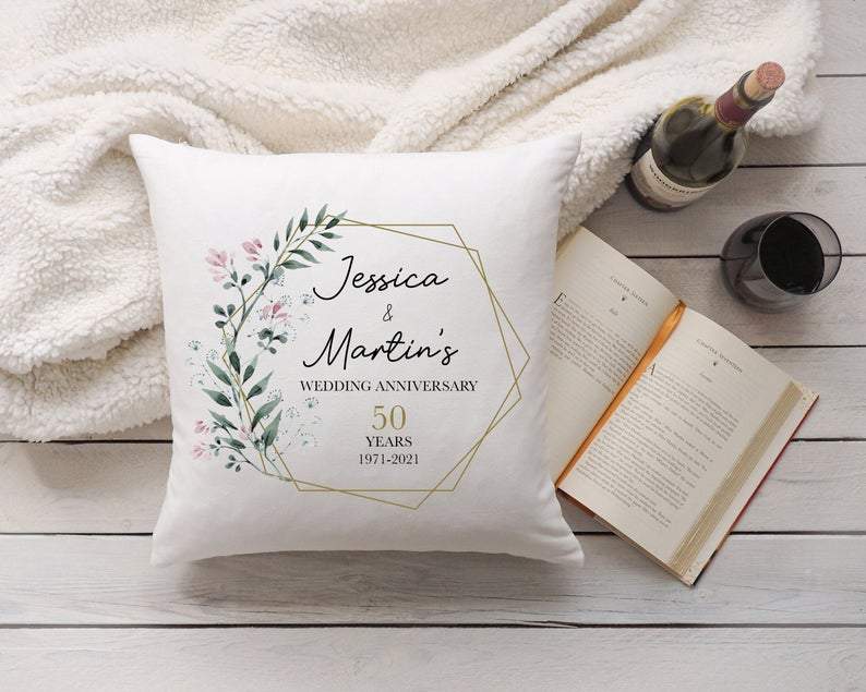 Decorative personalised pillow with 'Jessica & Martin's Wedding Anniversary' text on a wooden surface with a book and wine bottle.