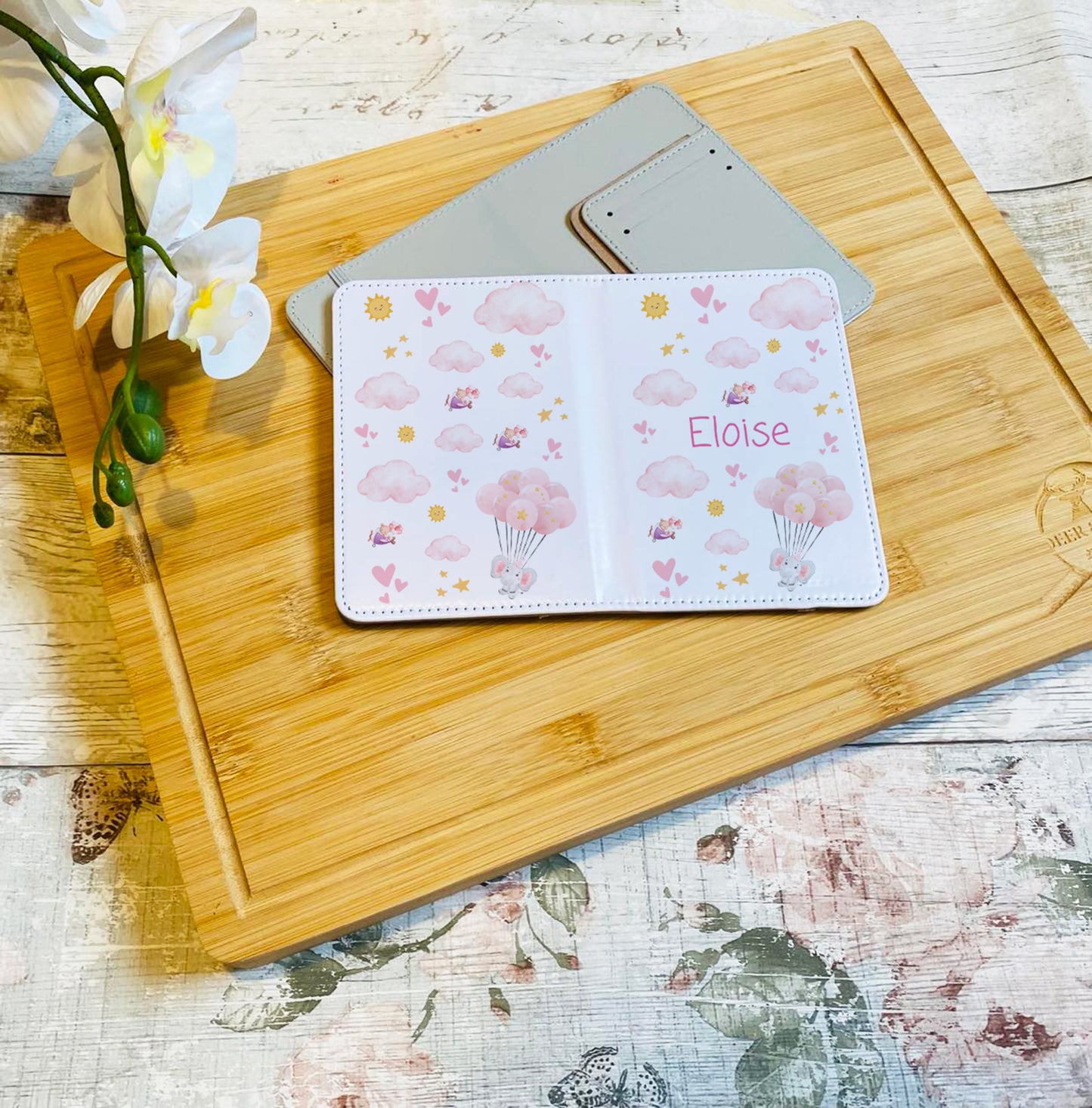 Personalised children's passport holders in a pink design with clouds, hearts, balloons, and custom names, for girls.