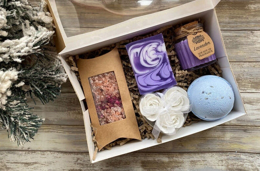 Gift set with bath products including a purple soap, lavender bath bomb, and bath salts on a wooden surface.