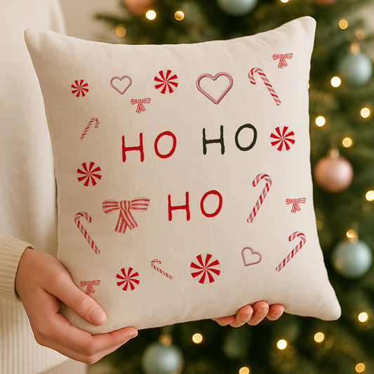 Beige pillow with 'HO HO HO' text and festive patterns held in front of a decorated Christmas tree.