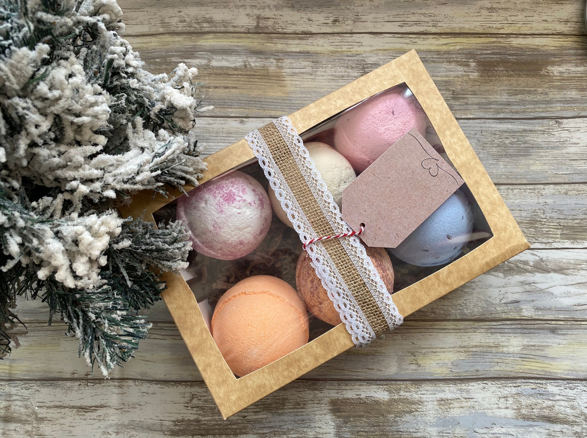 Box of bath bombs with a decorative tag on a wooden surface next to a small Christmas tree.