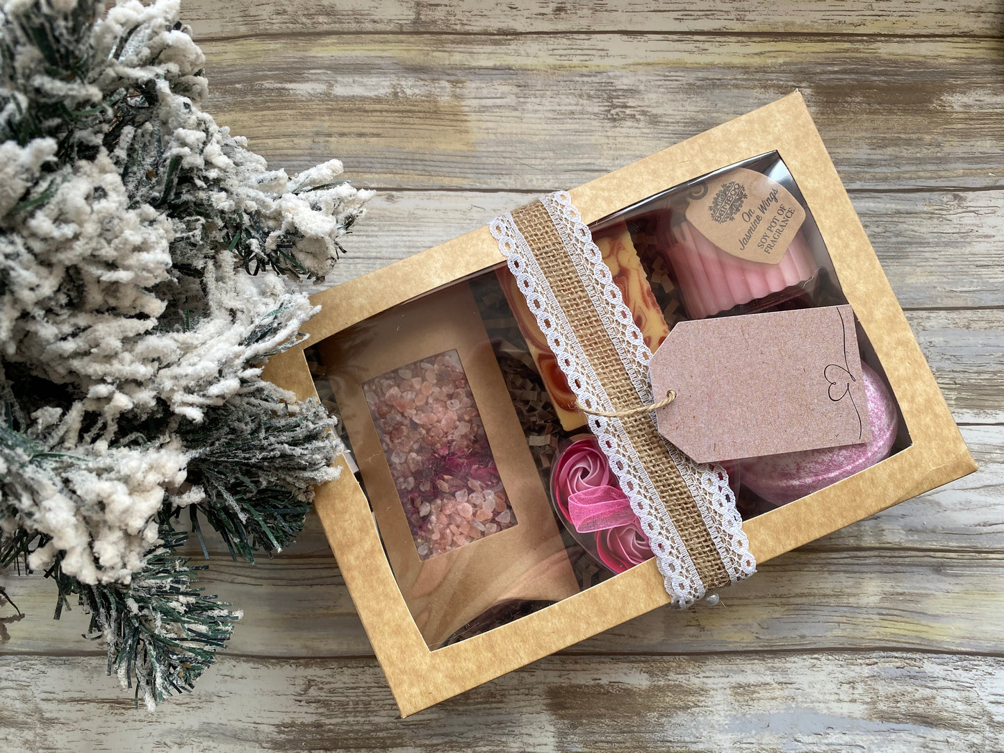 Gift box with decorative items on a wooden surface next to a small Christmas tree.