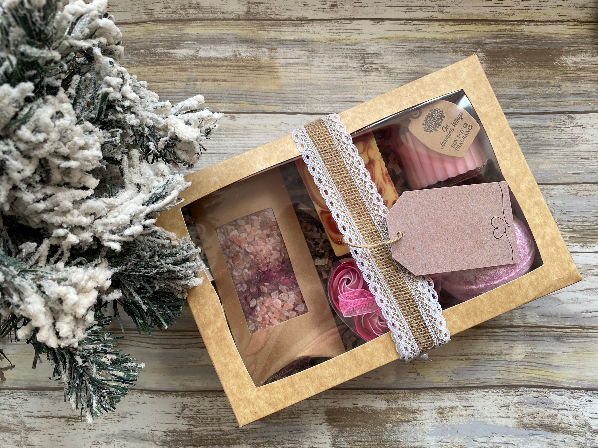 Gift box with decorative items on a wooden surface next to a small Christmas tree.