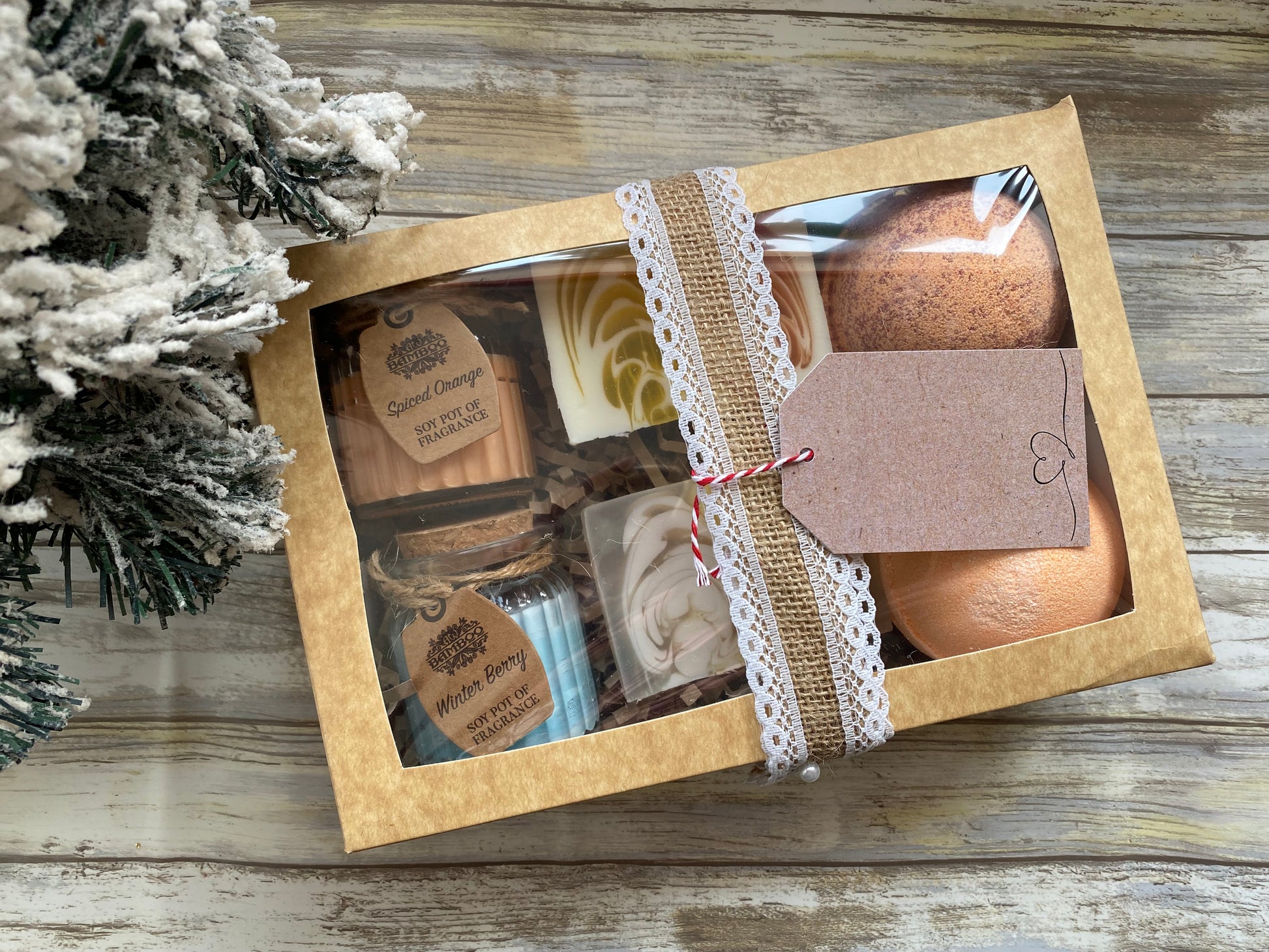 Gift set with bath bombs and soaps in a brown box on a wooden surface with a Christmas tree.