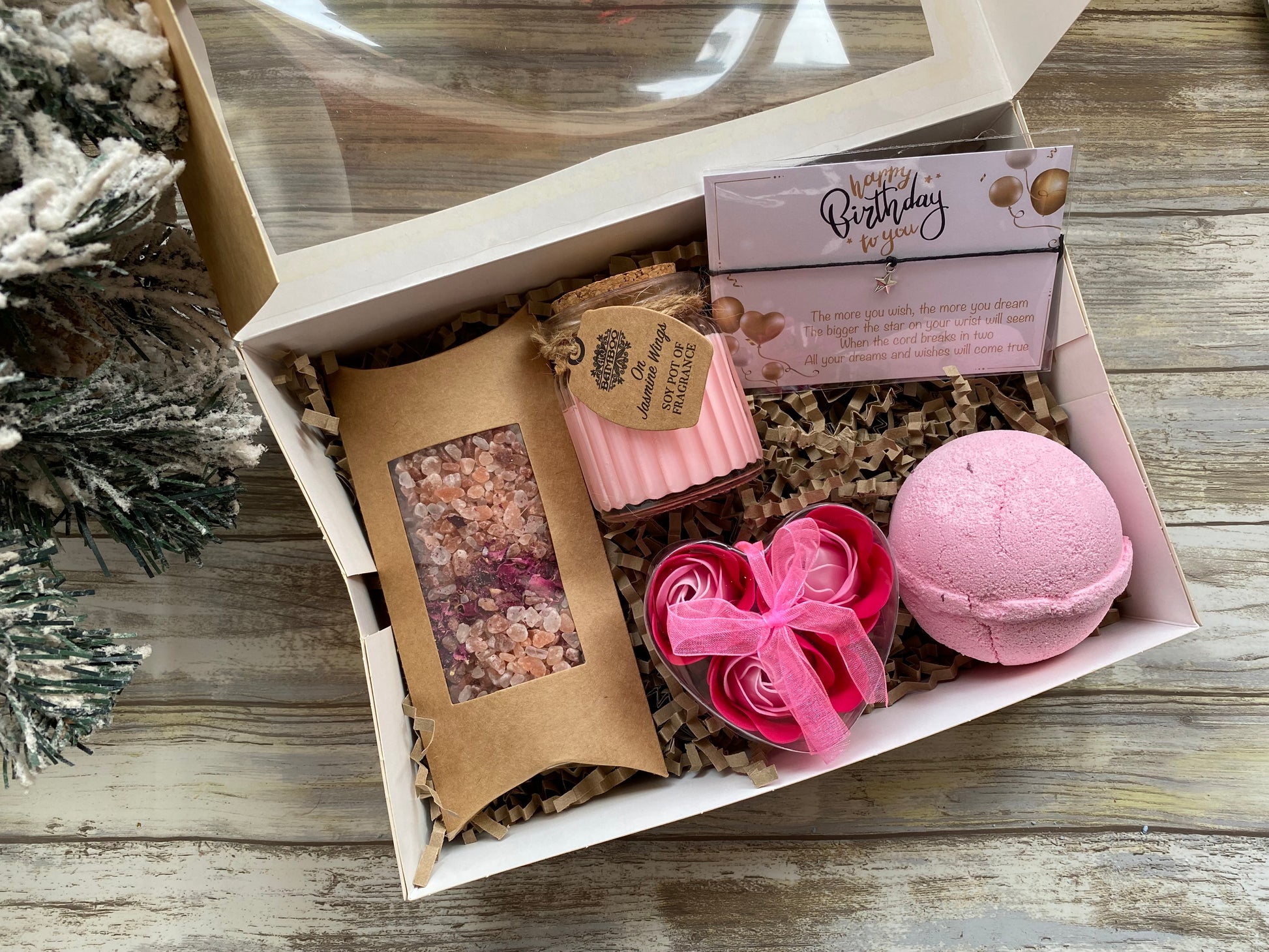 Gift box with bath products including a bath bomb, soap, and bath salts on a wooden surface.