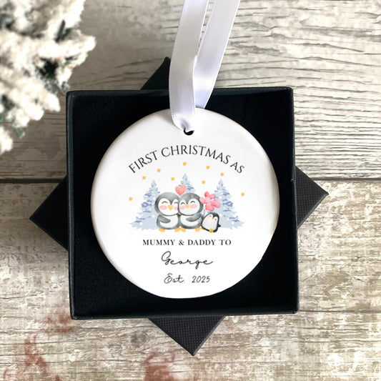 Decorative ornament for first Christmas with text and baby illustration, placed in a black box on a wooden surface.