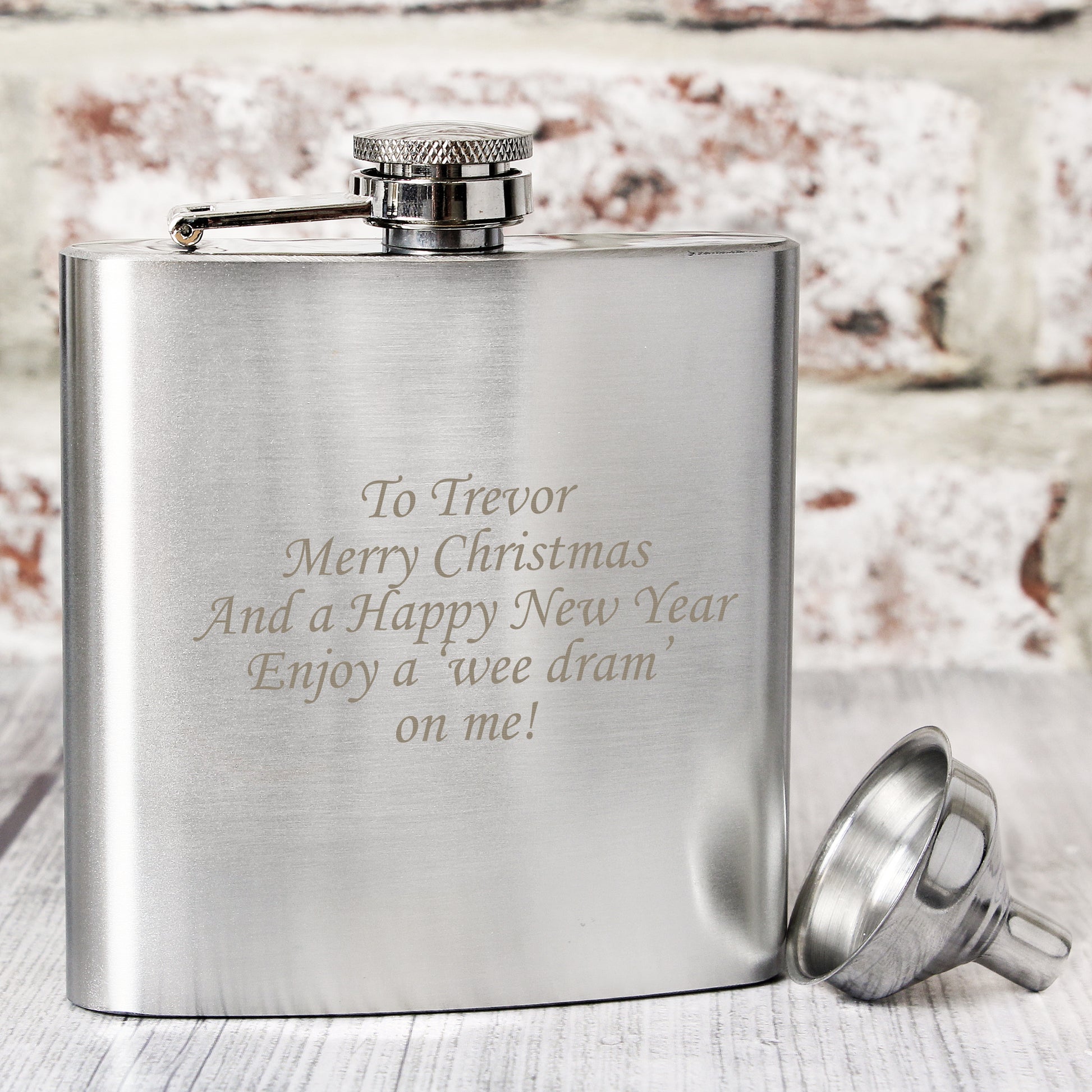 Silver hip flask with engraved text on a wooden surface