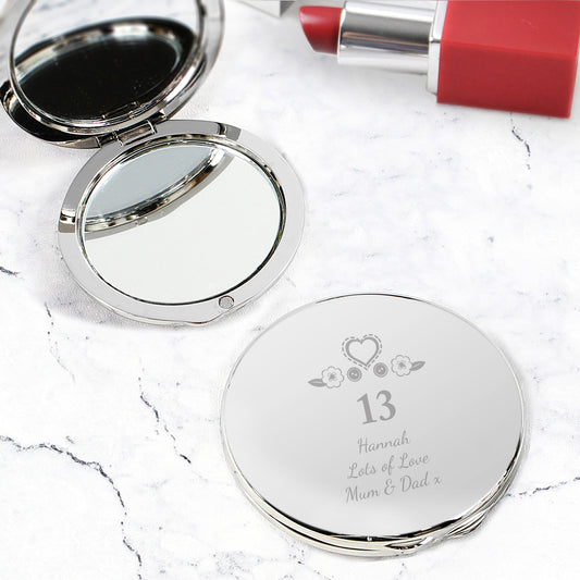 Compact mirror with engraved text on a marble surface with a red lipstick.