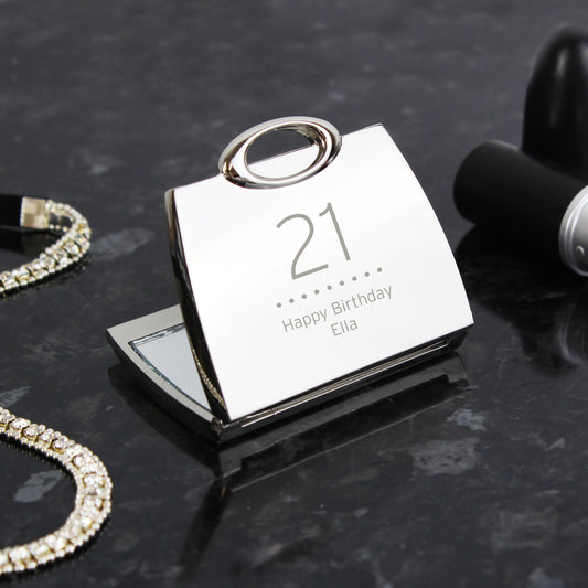Silver mirror with '21 Happy Birthday Ella' text on a dark surface with jewellery.