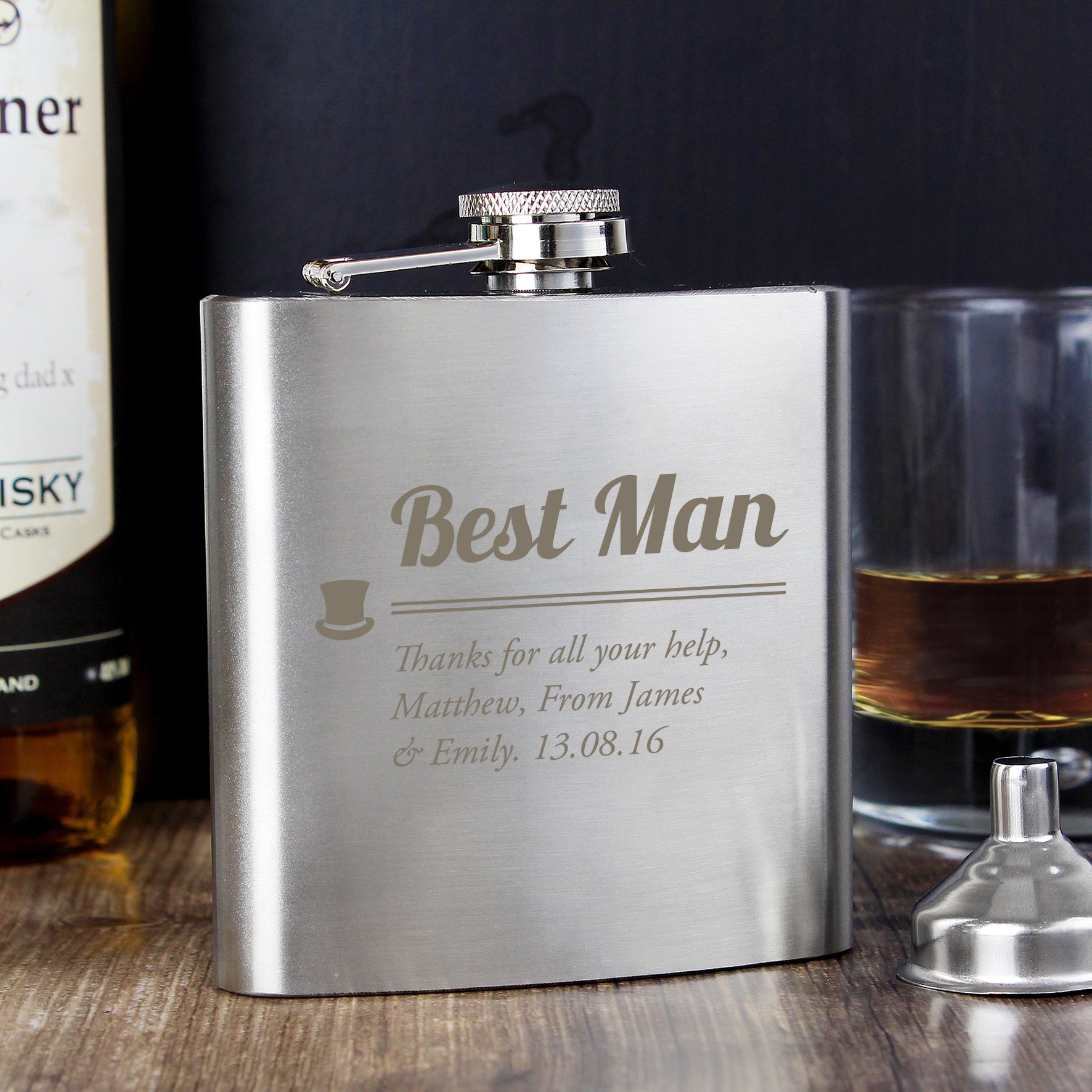 Stainless steel flask engraved with 'Best Man' message on a wooden surface with a bottle and glass in the background.