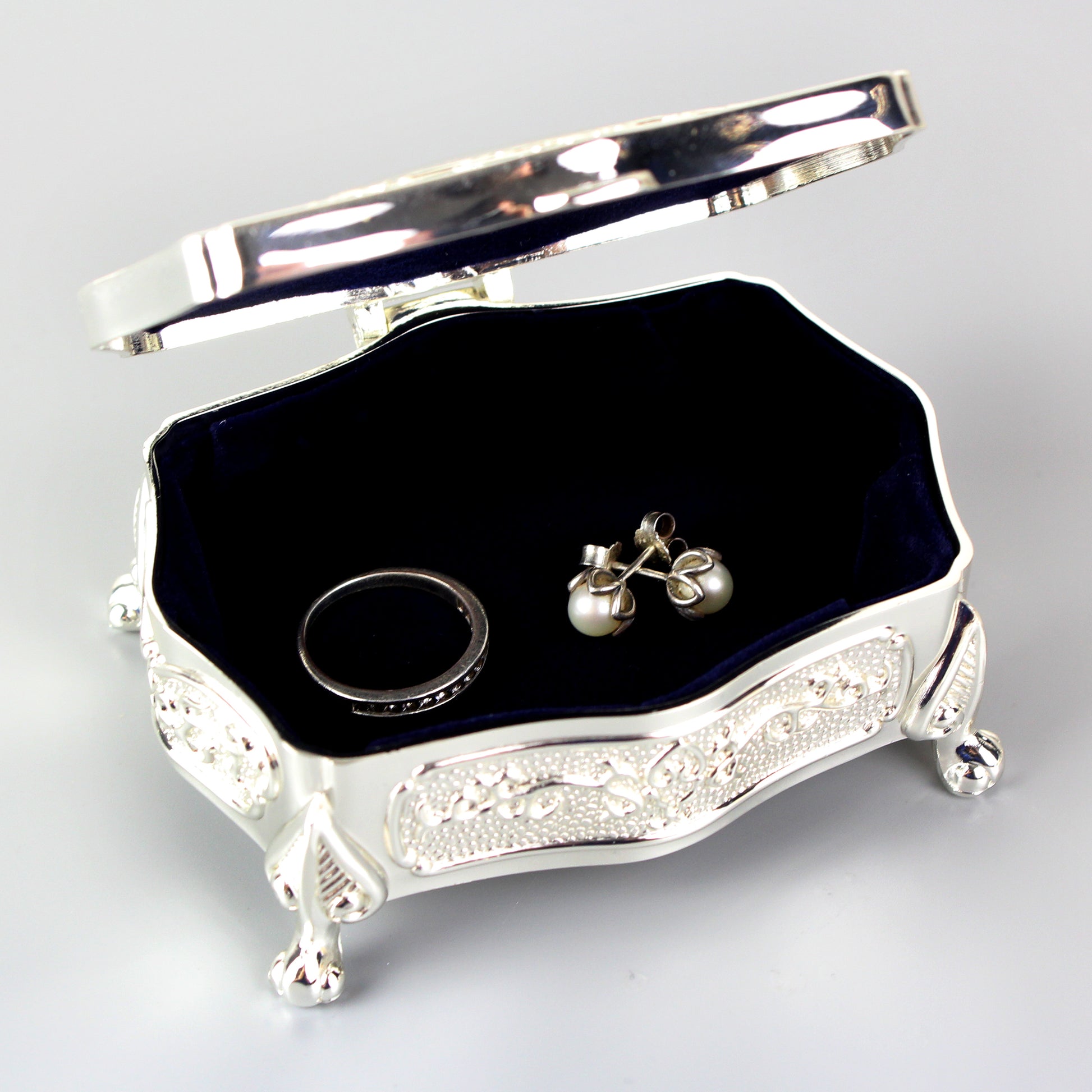 Silver jewelry box with a black interior containing a ring and earrings on a light gray background