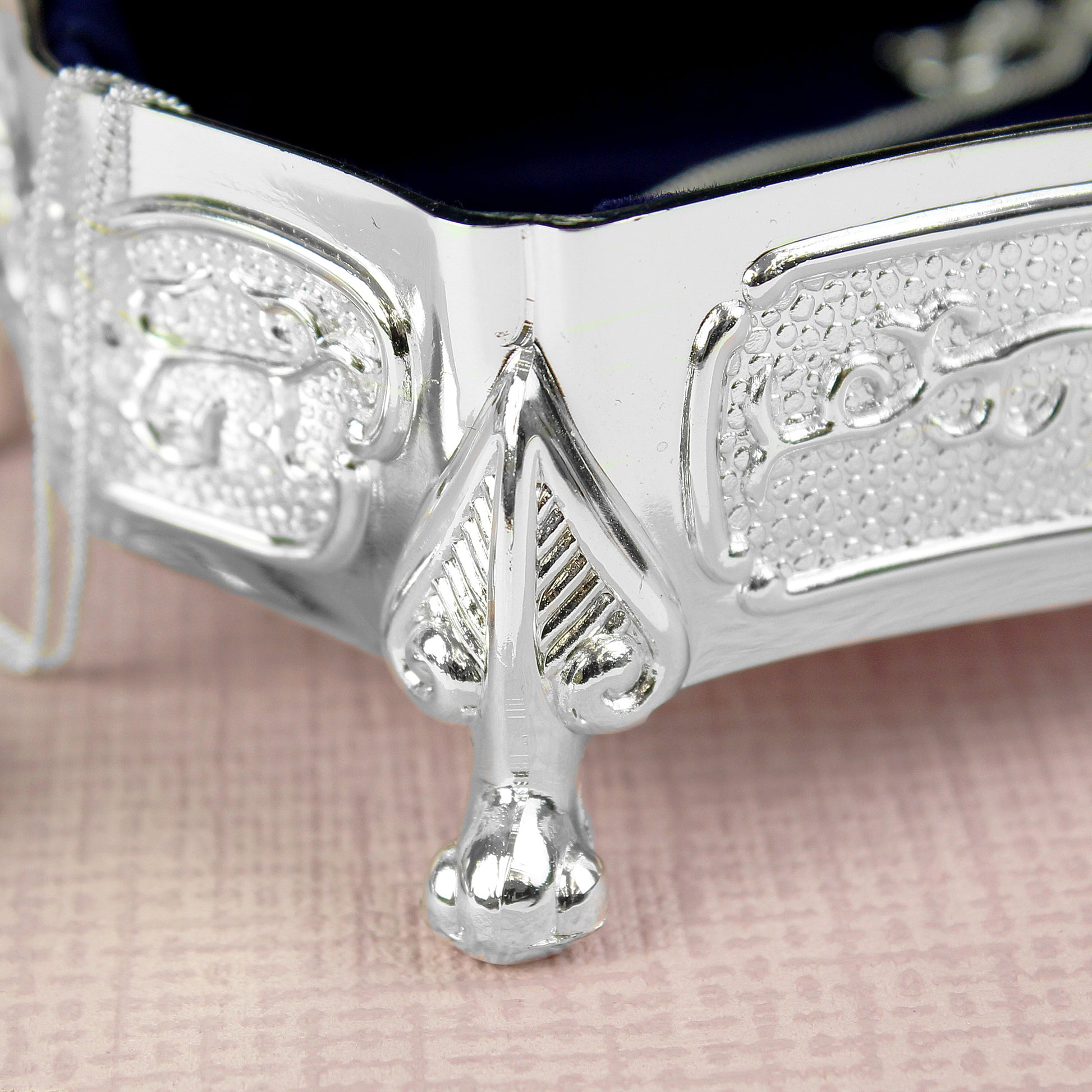 Close-up of a silver box with intricate designs on a pink fabric background