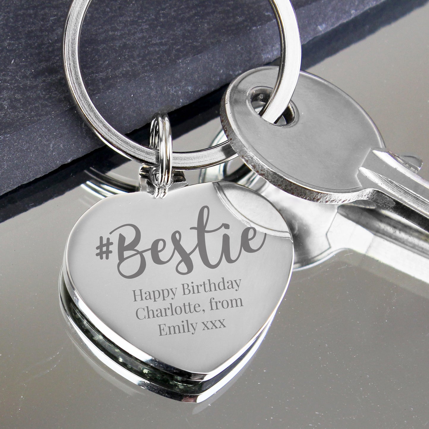 Silver keychain with heart-shaped tag engraved with '#Bestie' and personalised message on a reflective surface.