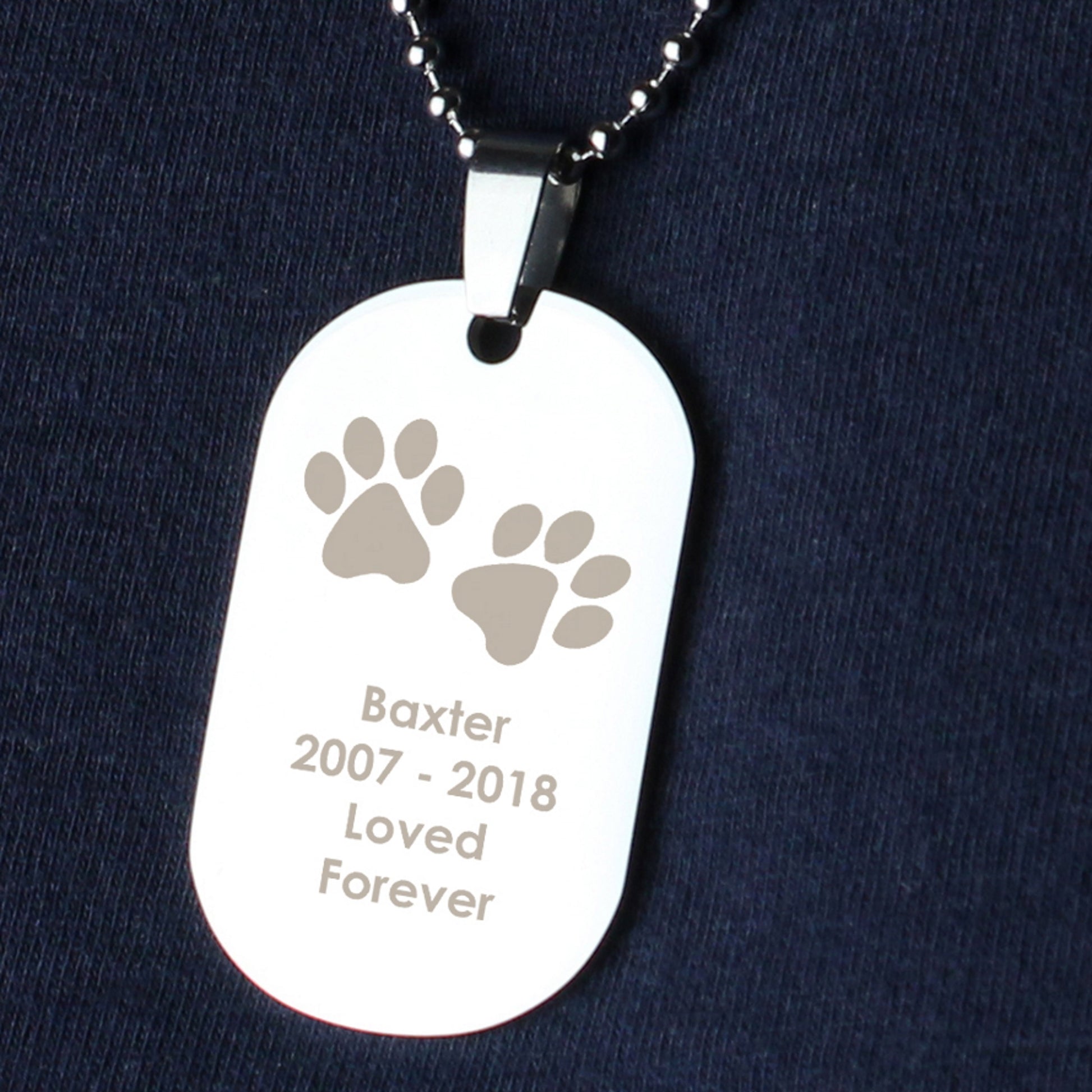 Dog tag necklace with engraved paw prints and text on a dark background