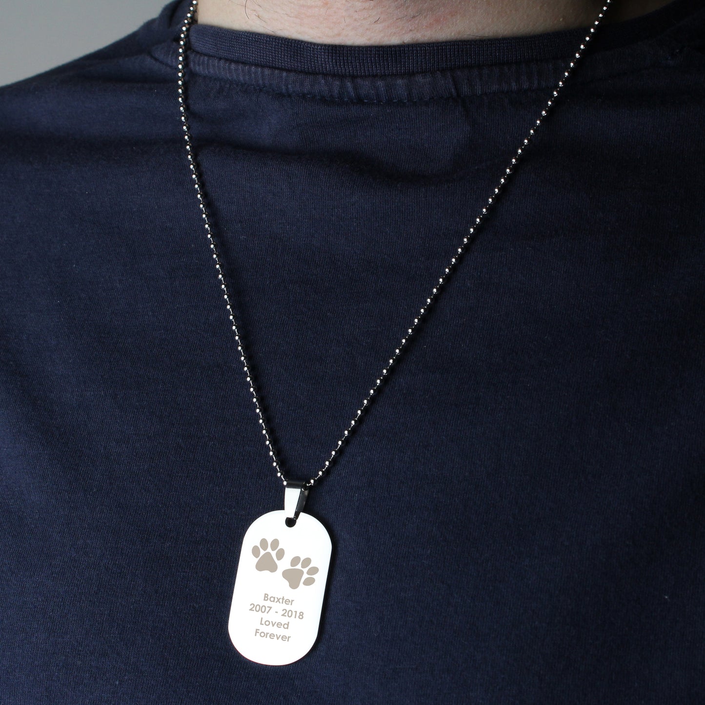 Dog tag necklace with engraved text on a person wearing a dark blue shirt