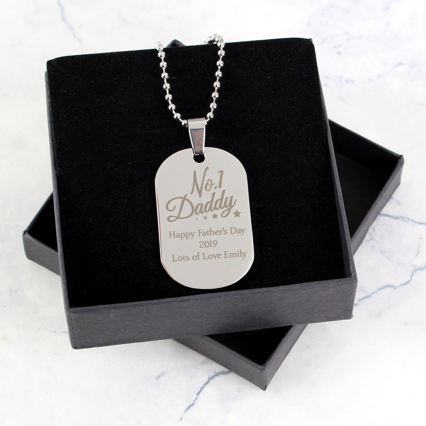 Silver dog tag necklace with engraved text in a black box on a light gray background