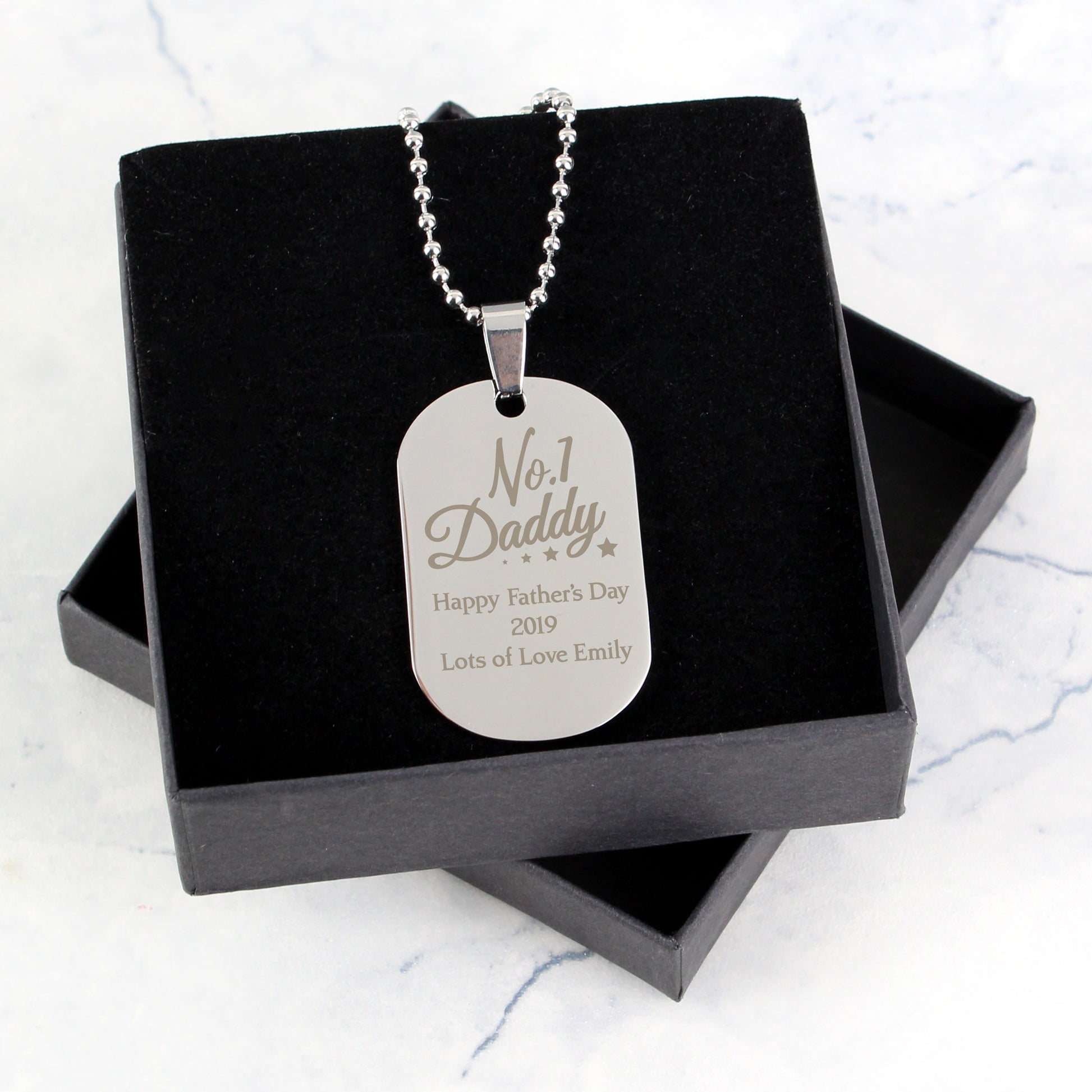 Silver dog tag necklace with engraved text in a black box on a light gray background