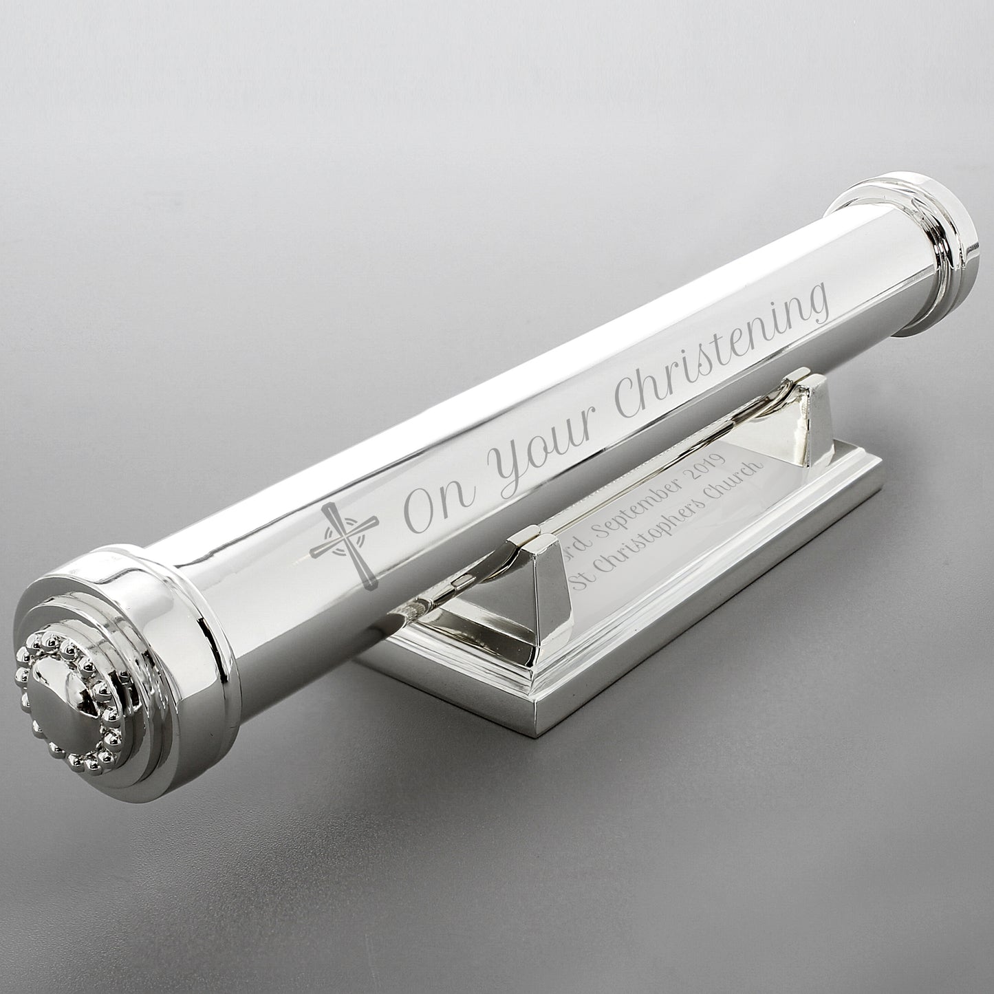 Silver christening candle holder with engraved text on a grey background