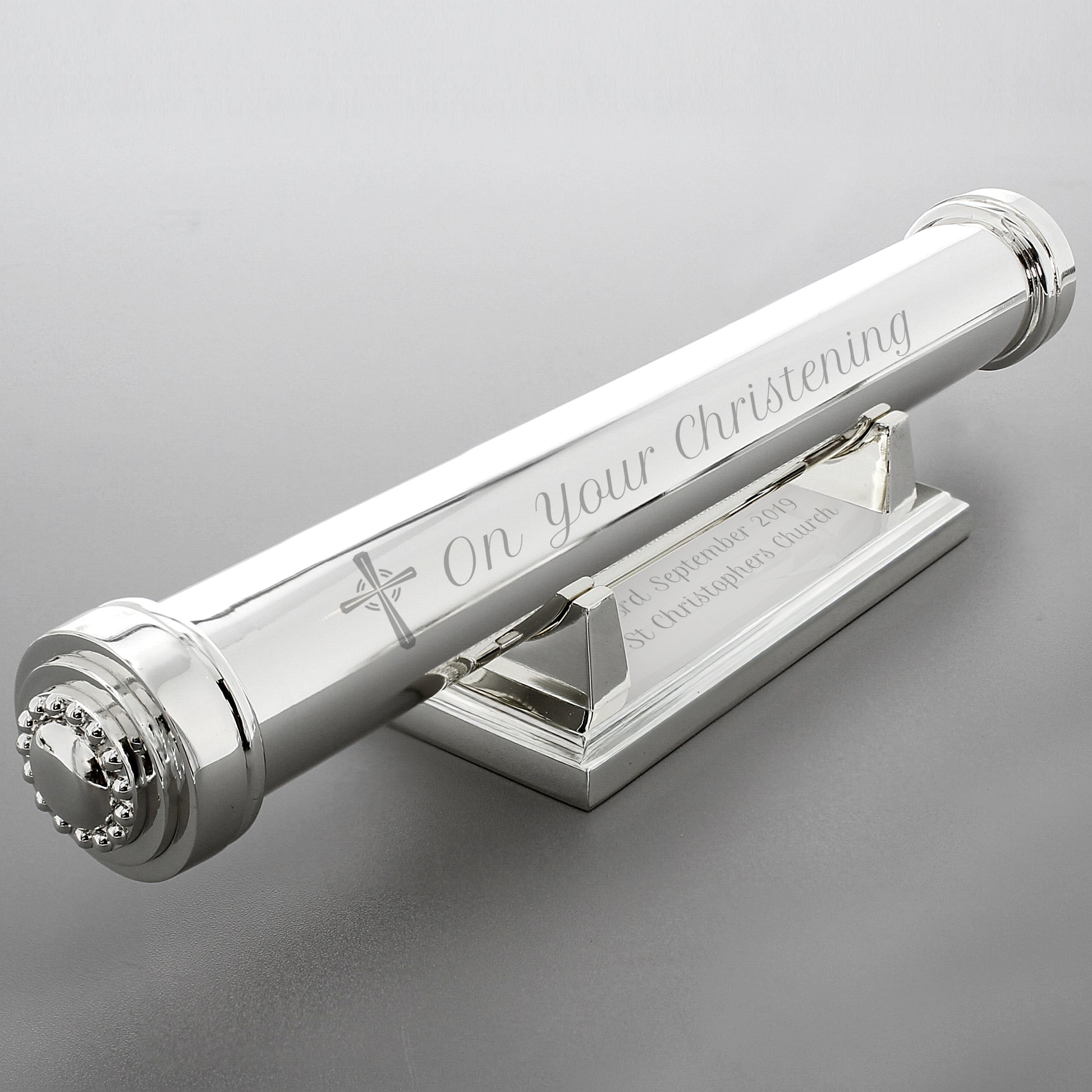 Silver christening candle holder with engraved text on a grey background