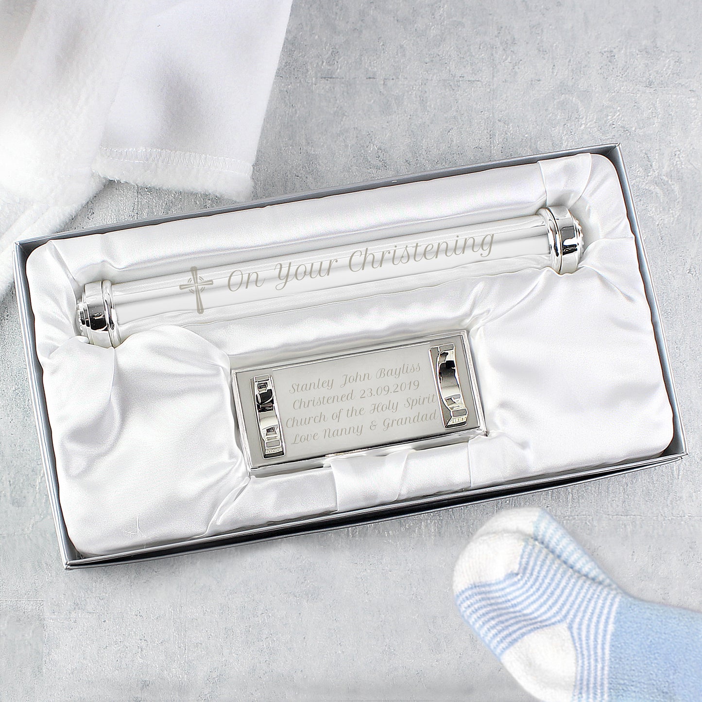 Silver christening certificate holder in a box with a white sock on a light grey background