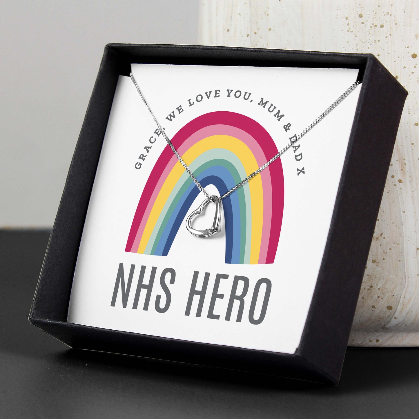 Necklace with heart pendant on a card featuring a rainbow and text, in a black box.