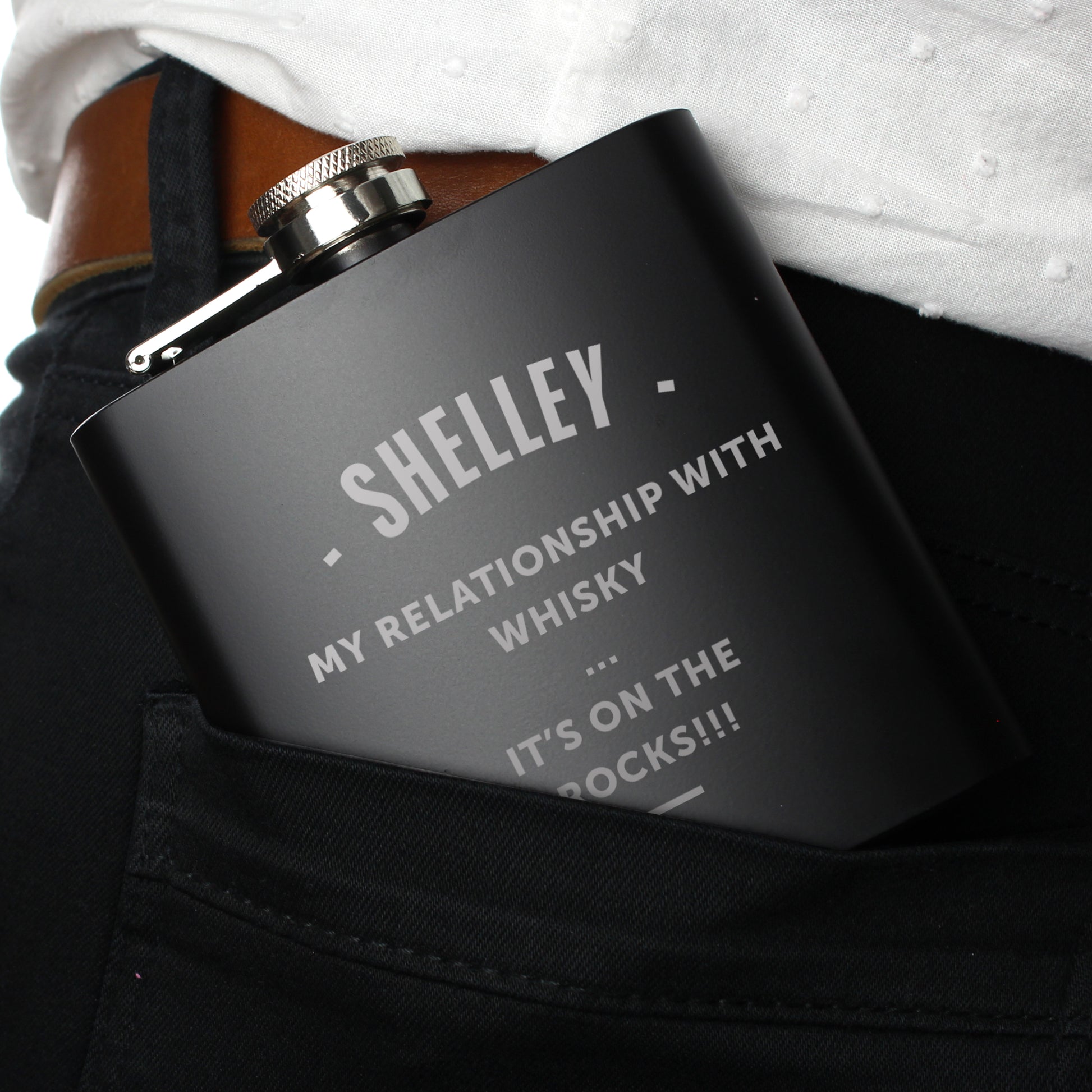 Black flask with engraved text held in a person's pocket