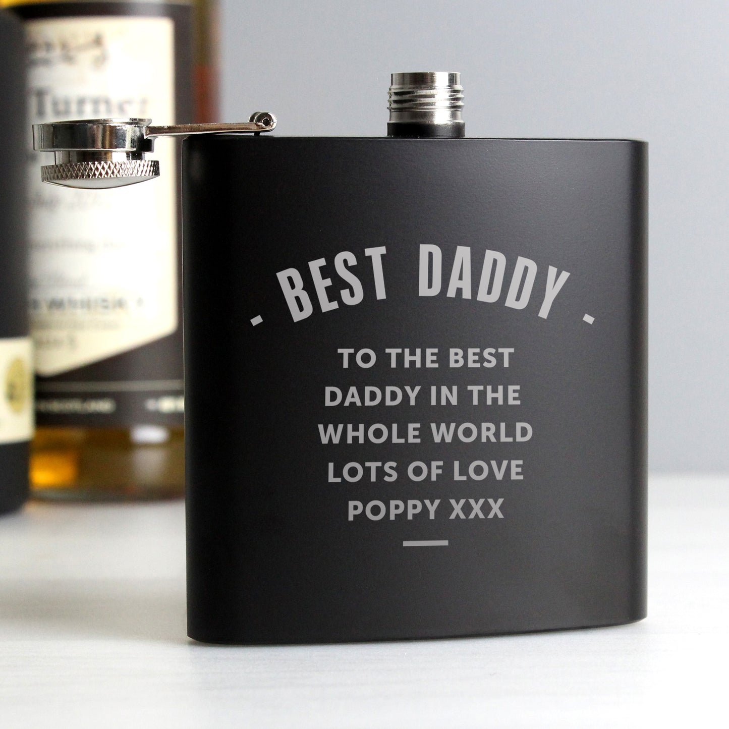 Black flask with engraved message on a light grey background
