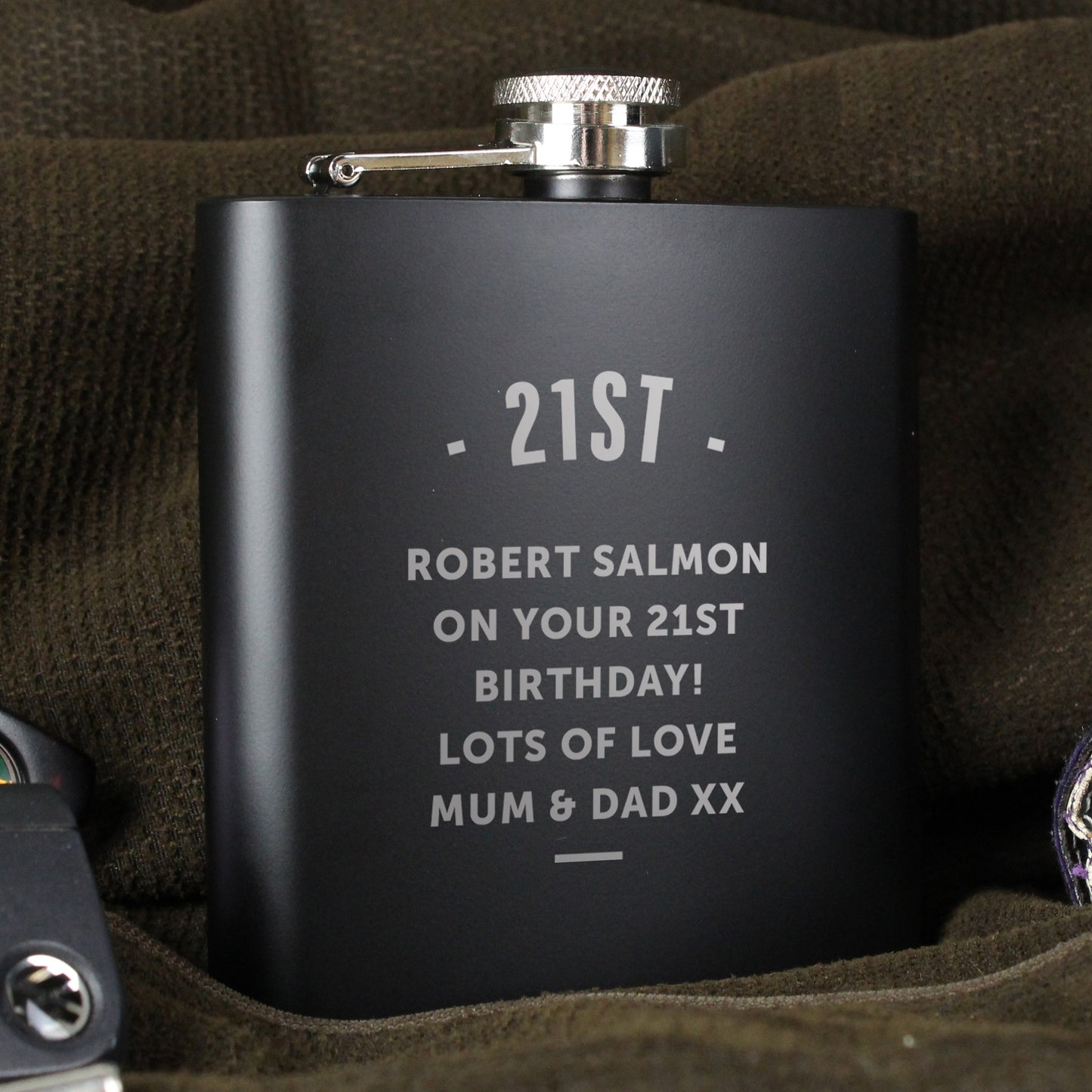 Black flask with engraved text on a brown fabric background