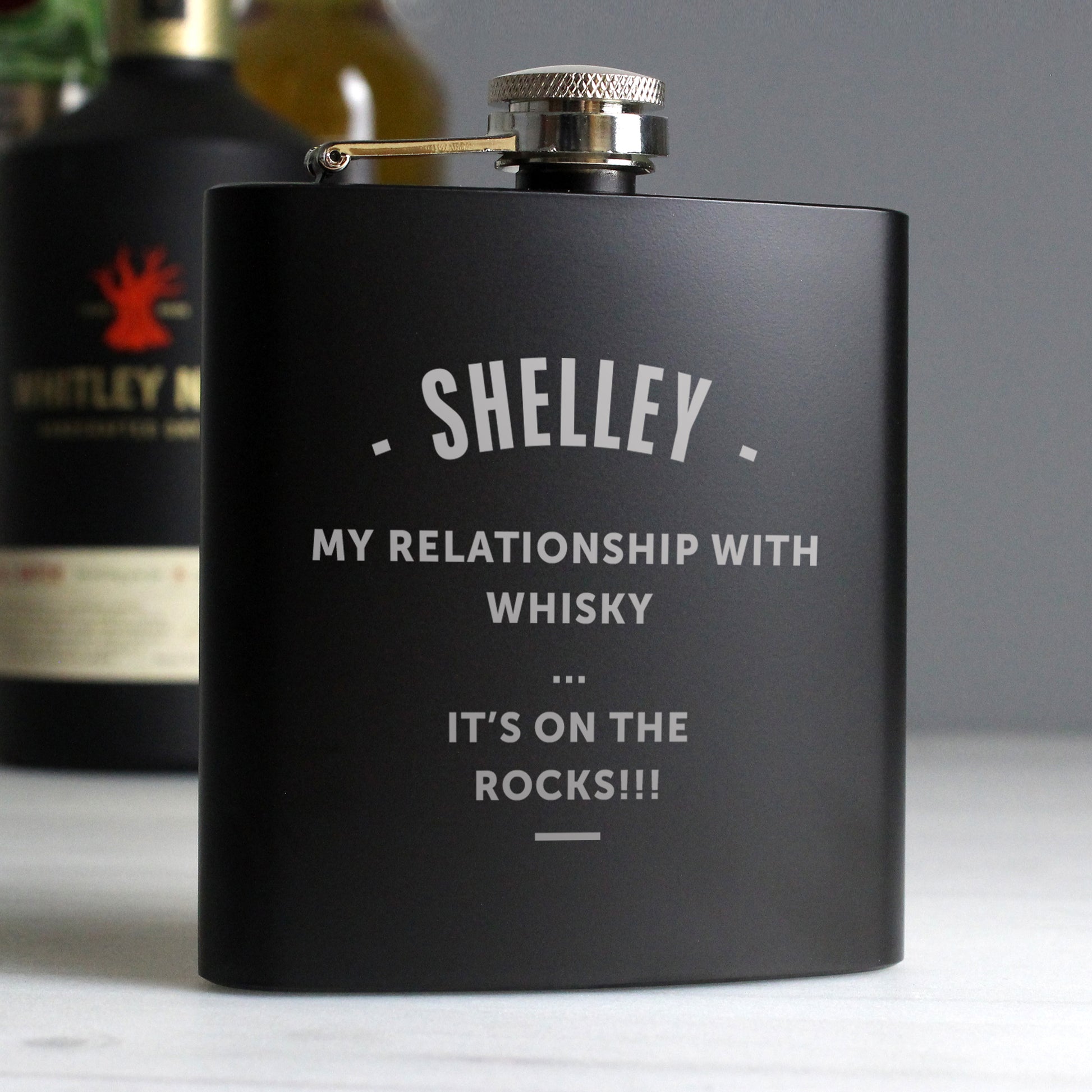 Black flask with humorous text about whisky relationship on a grey background