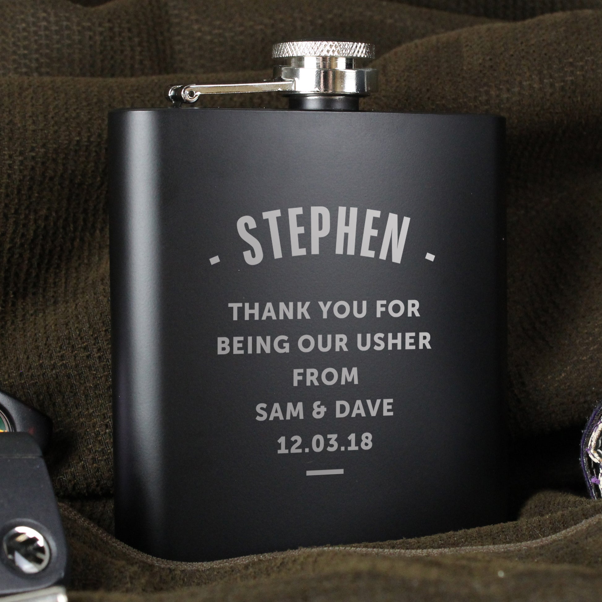 Black flask with engraved text on a brown fabric background