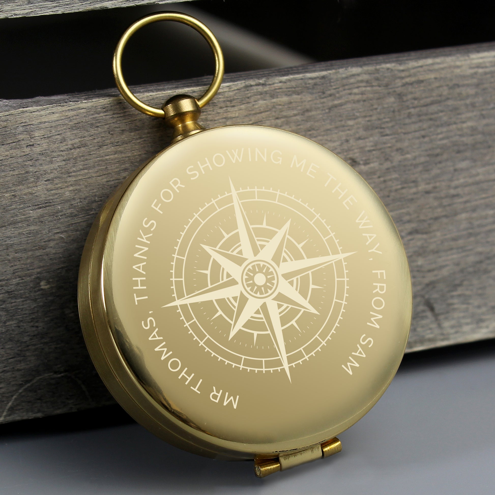 Personalised Gold compass with engraved text on a wooden surface