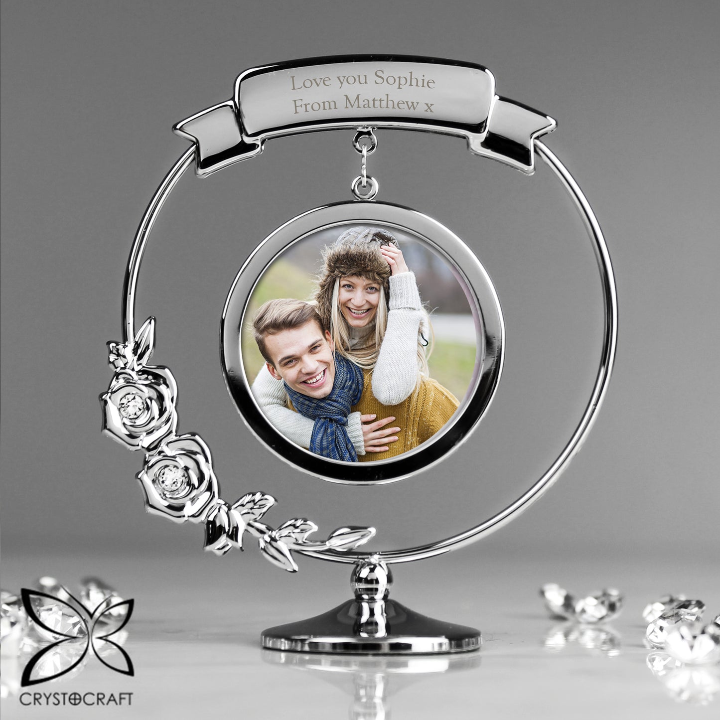 Silver photo frame with a circular design, featuring a couple's photo and engraved text, on a grey background.