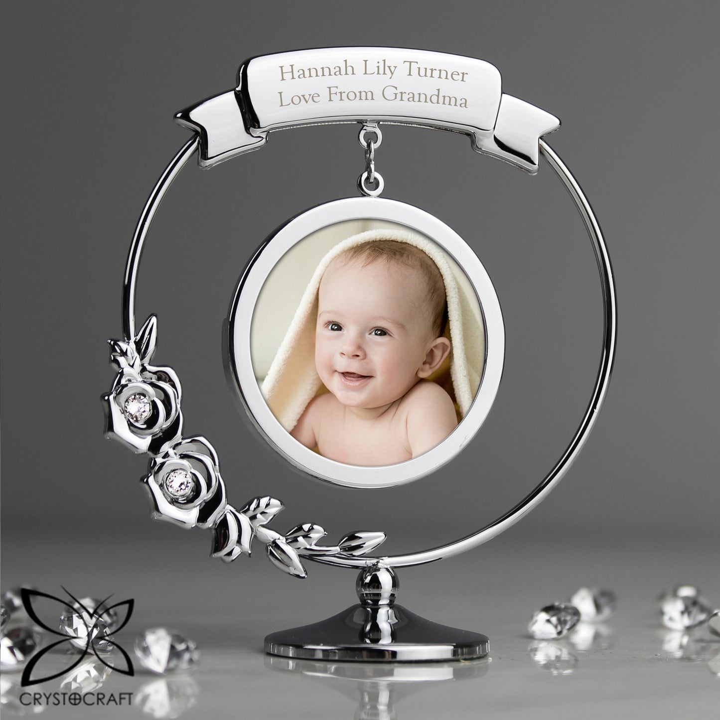 Silver photo frame with a baby's picture and 'Love From Grandma' engraving on a grey background.