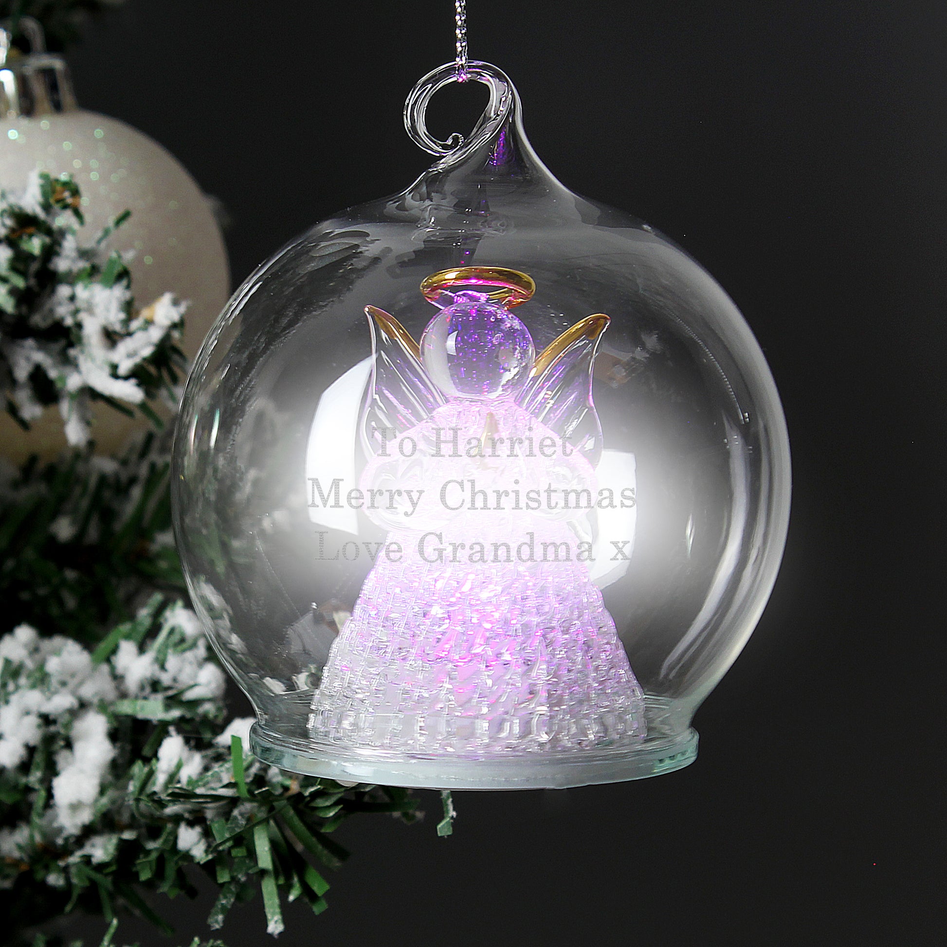 Decorative angel ornament in a glass ball with personalized text, against a dark background.