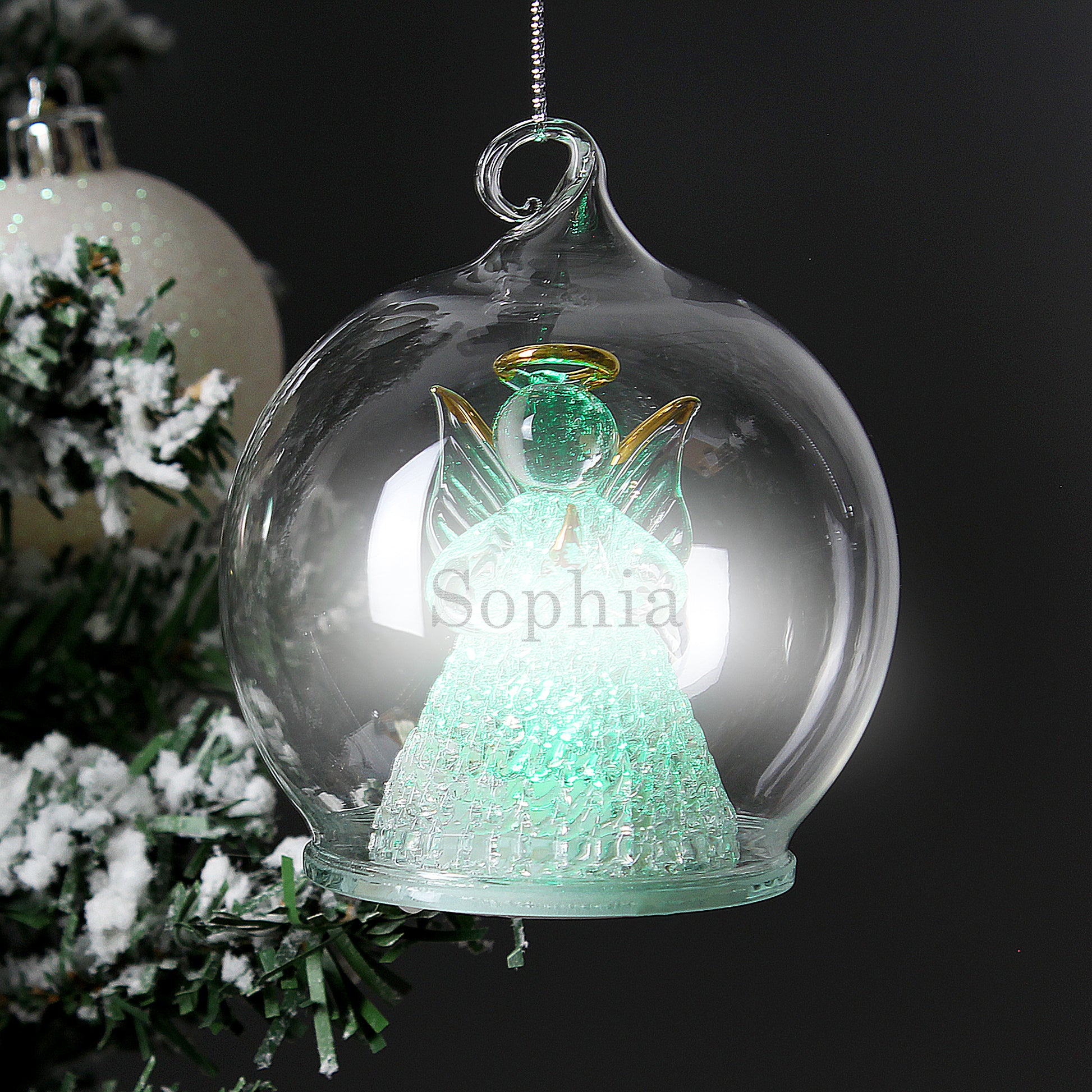 Decorative angel ornament with 'Sophia' inside a glass bubble, Christmas tree in the background