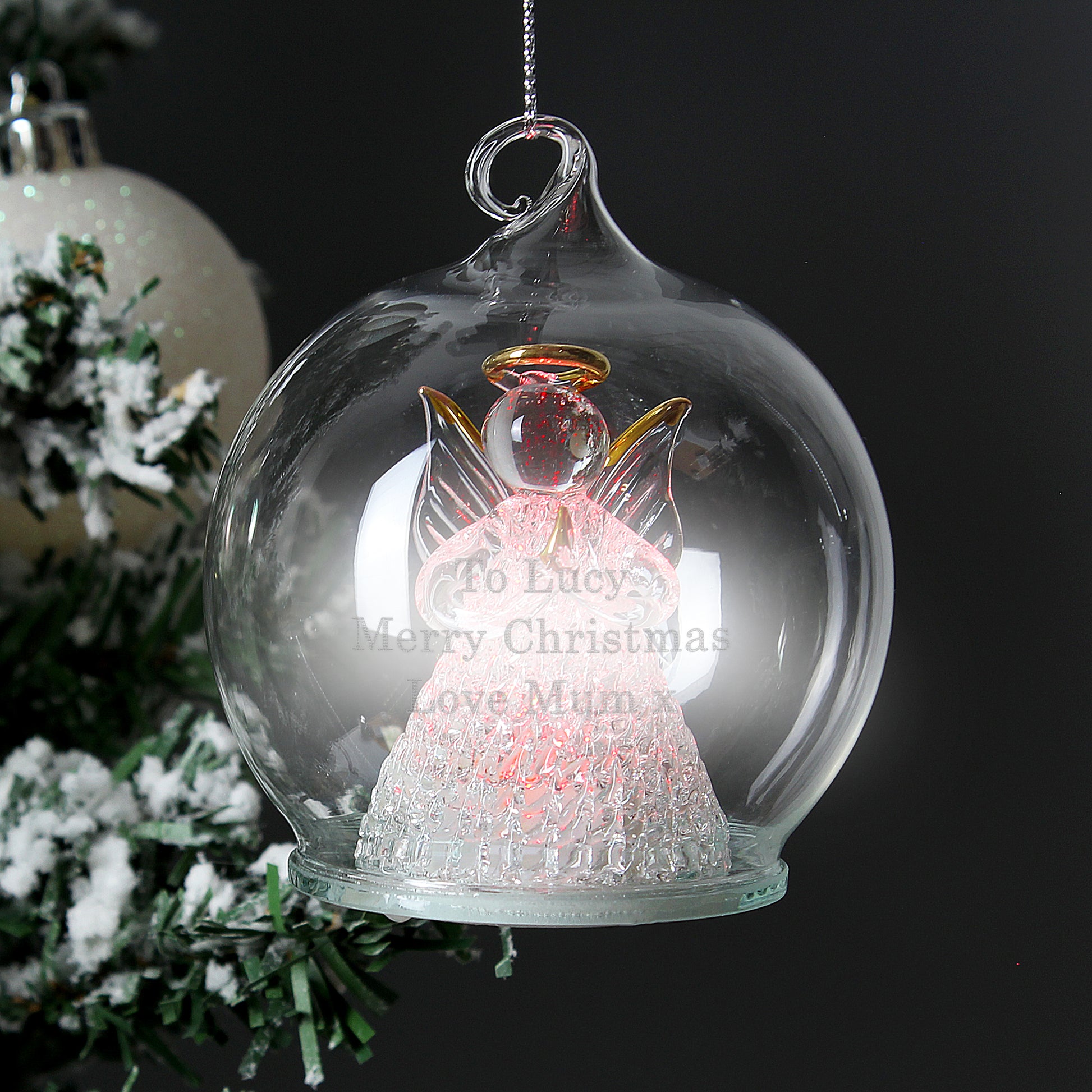 Decorative angel ornament in a glass bubble with text, Christmas tree in the background